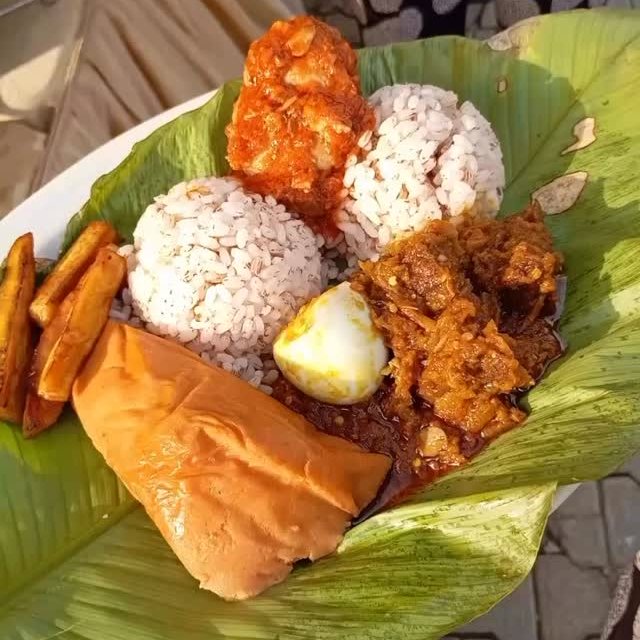 A plated Nigerian meal on a banana leaf: ofada rice, moi moi, plantain, egg and stew
